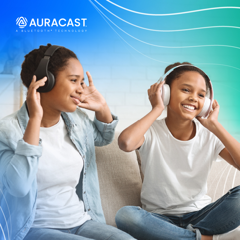 Young girls joyfully listening to music with AURACAST Bluetooth headphones on a cozy sofa.